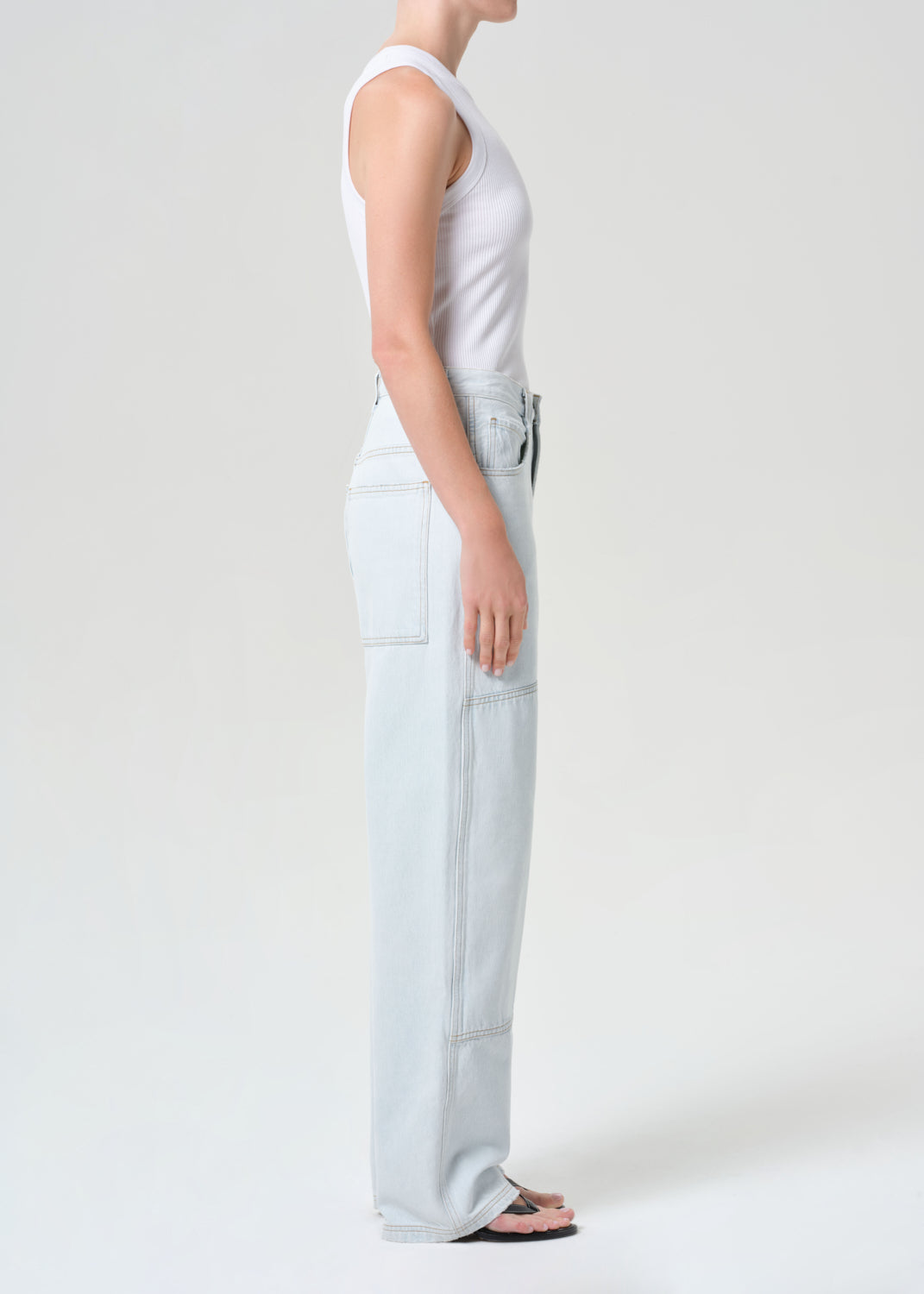 Person wearing a white sleeveless top and light blue jeans on a plain background