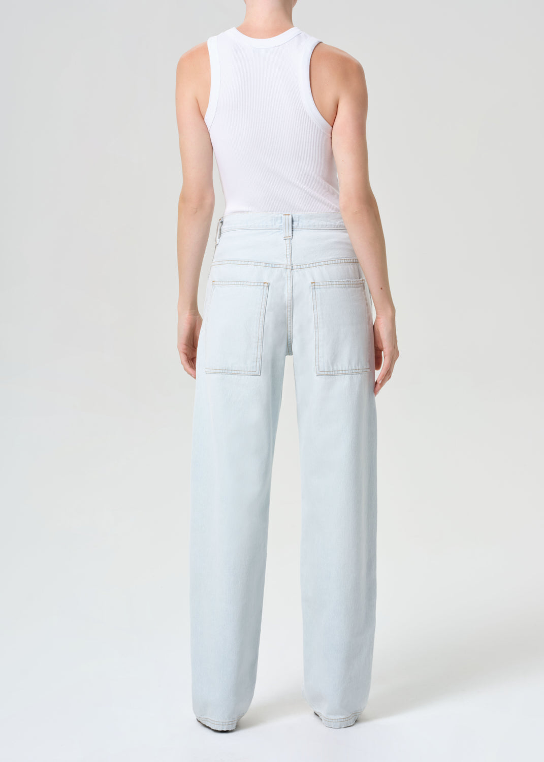 Person wearing light blue jeans and a white sleeveless top on a white background