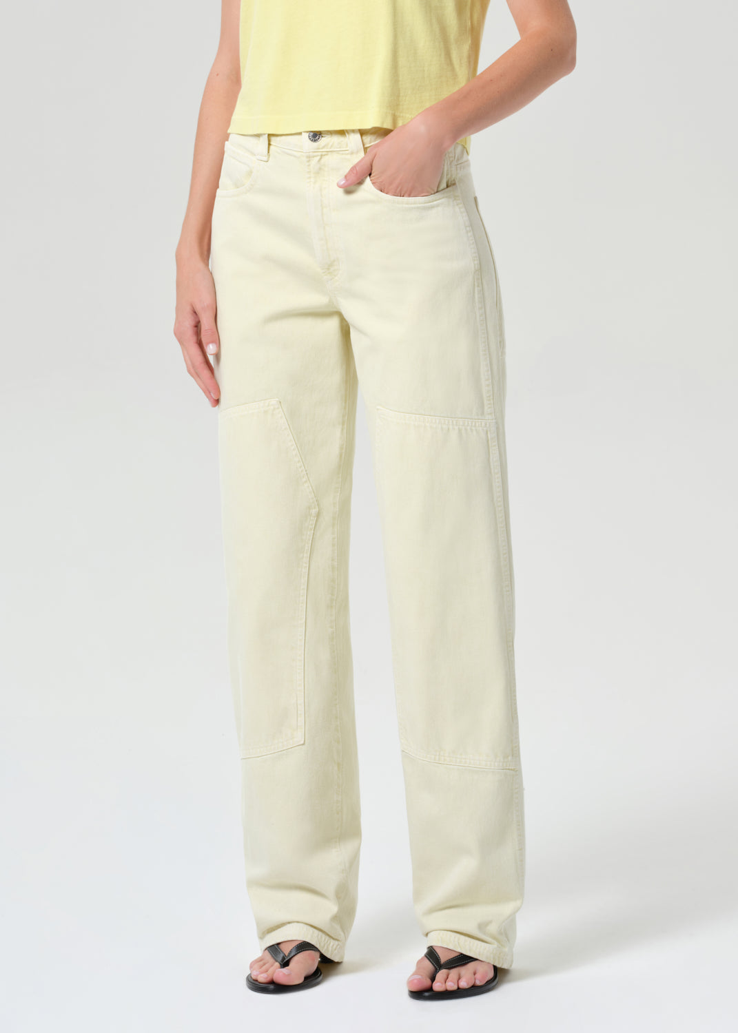 Person wearing light-colored pants and a yellow top on a white background