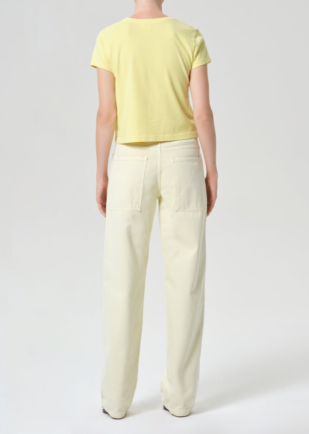 Person wearing a yellow top and light-colored pants on a white background