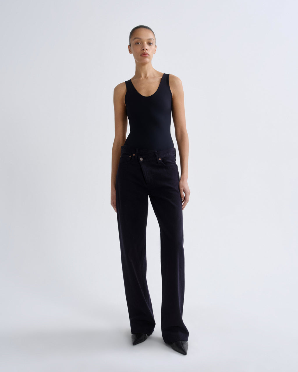 Person wearing a black sleeveless top and black pants on a grey background