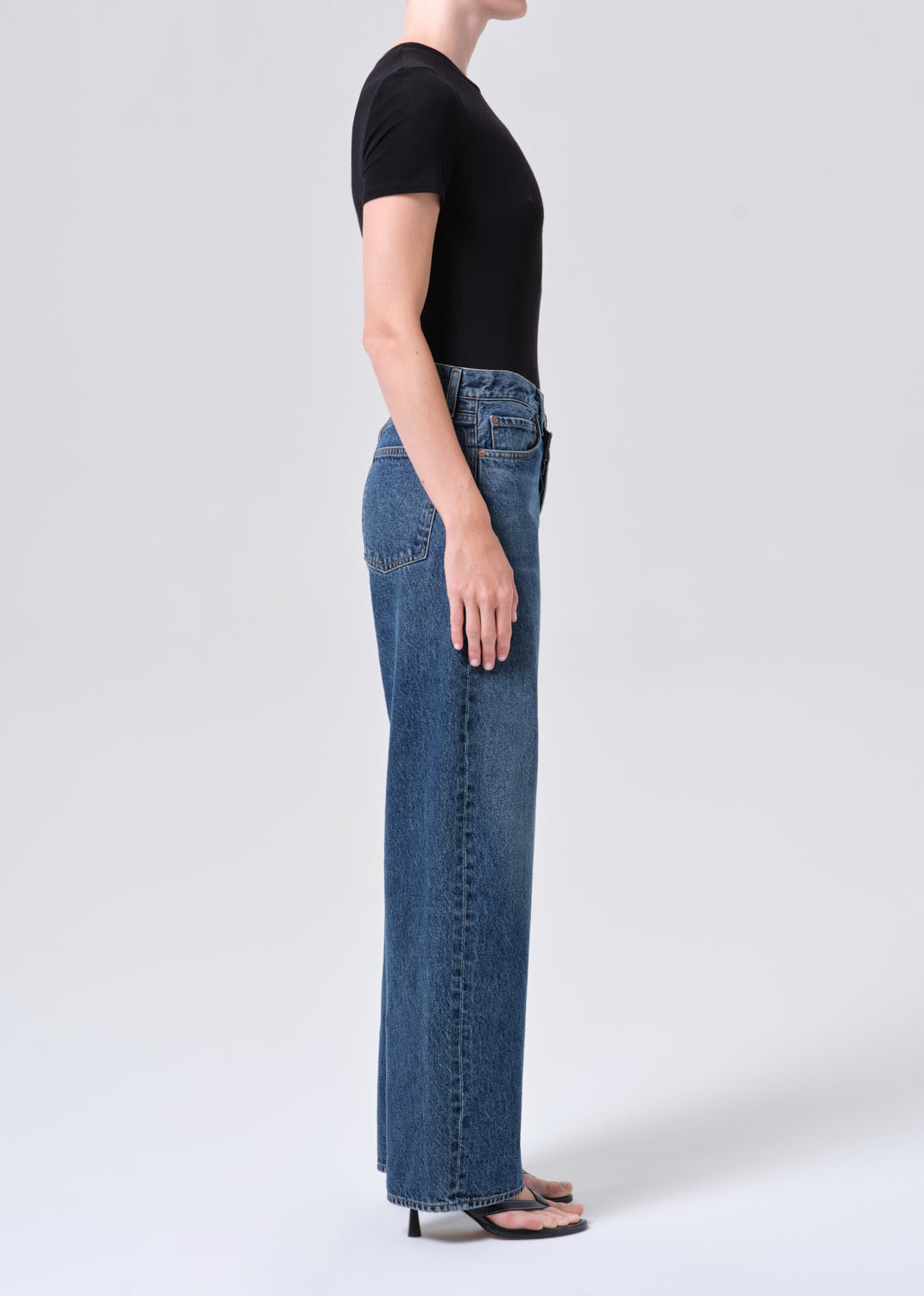 Person wearing blue jeans and a black top on a white background