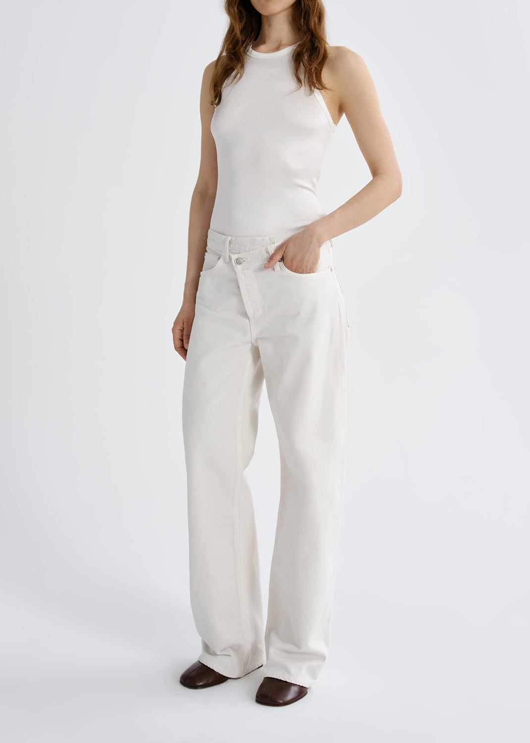 Person wearing a white tank top with white wide leg pants on a grey background