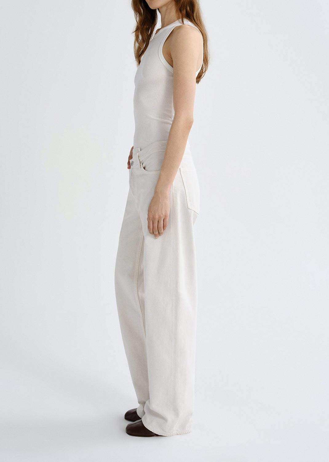 Person wearing a white tank top with white wide leg pants viewed from the side on a grey background