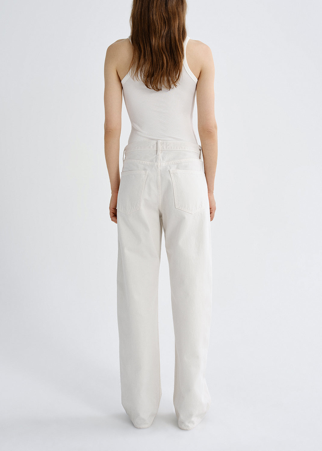 Person wearing a white tank top with white wide leg pants viewed from the back on a grey background