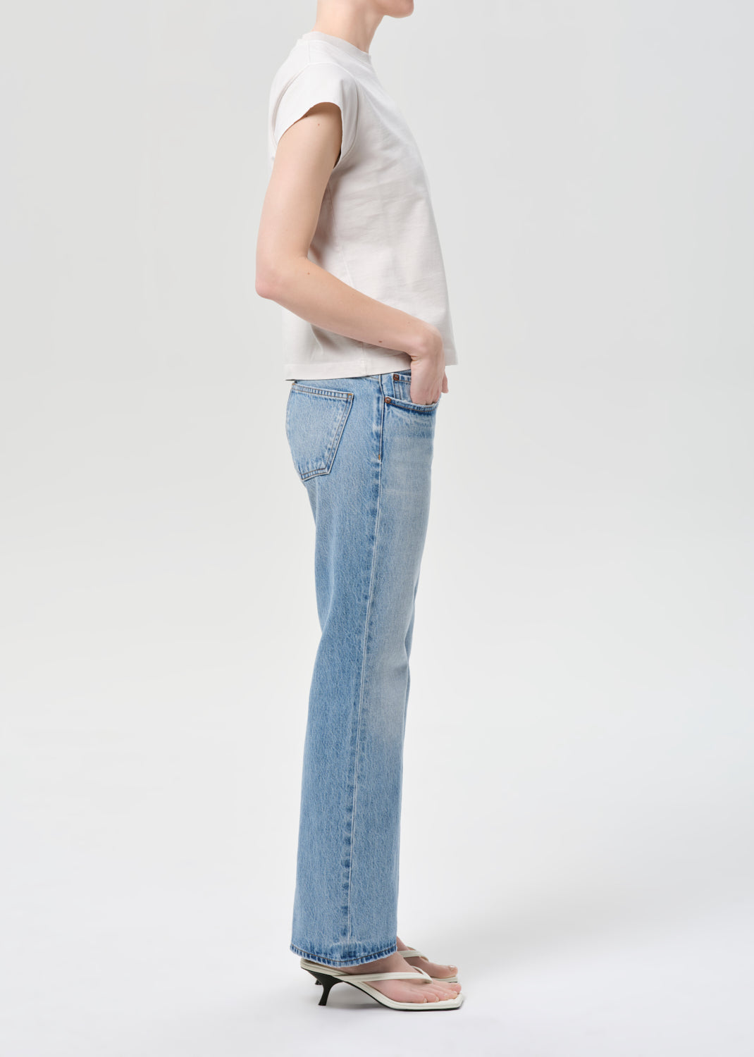 Person wearing a white t-shirt and light blue jeans on a plain background
