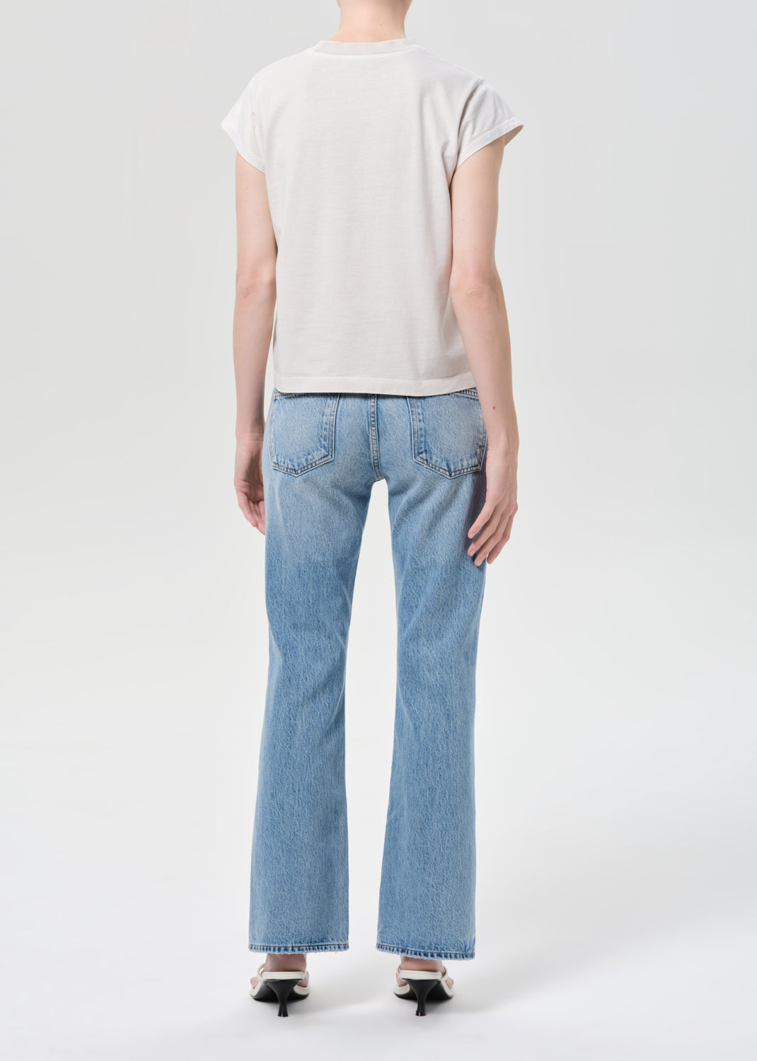 Person wearing light blue jeans and a white t-shirt on a plain background