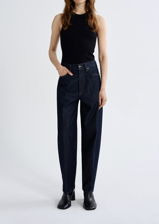Person wearing dark blue jeans and a black top on a grey background