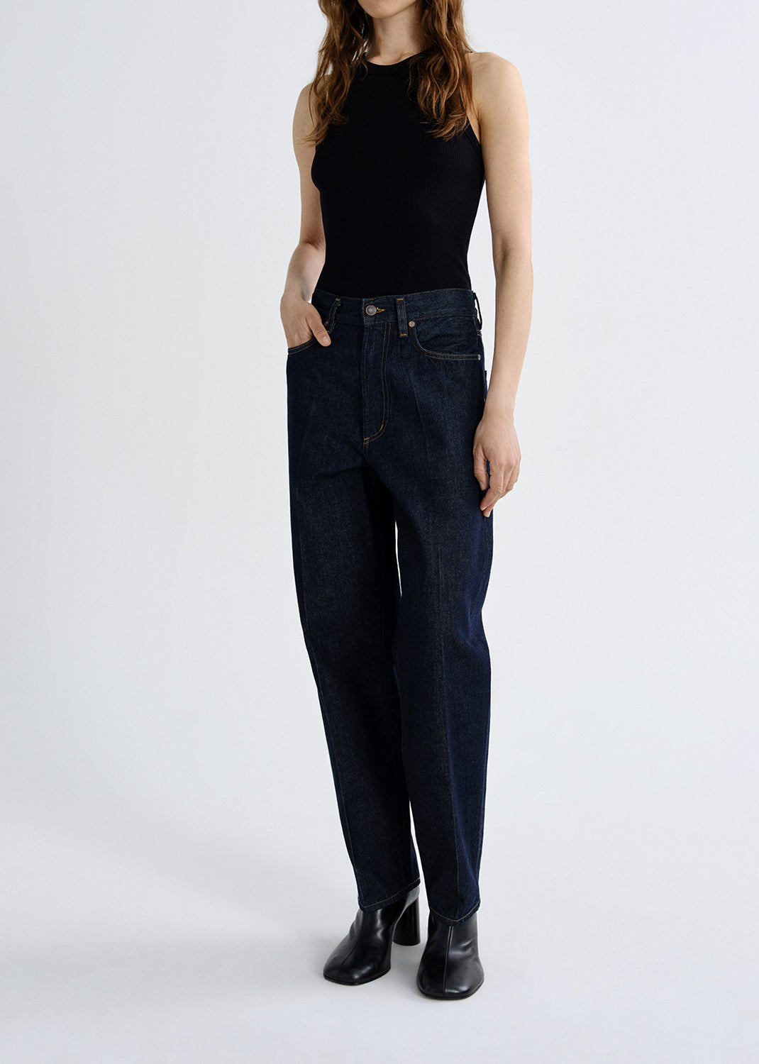 Person wearing dark blue jeans and a black top on a grey background