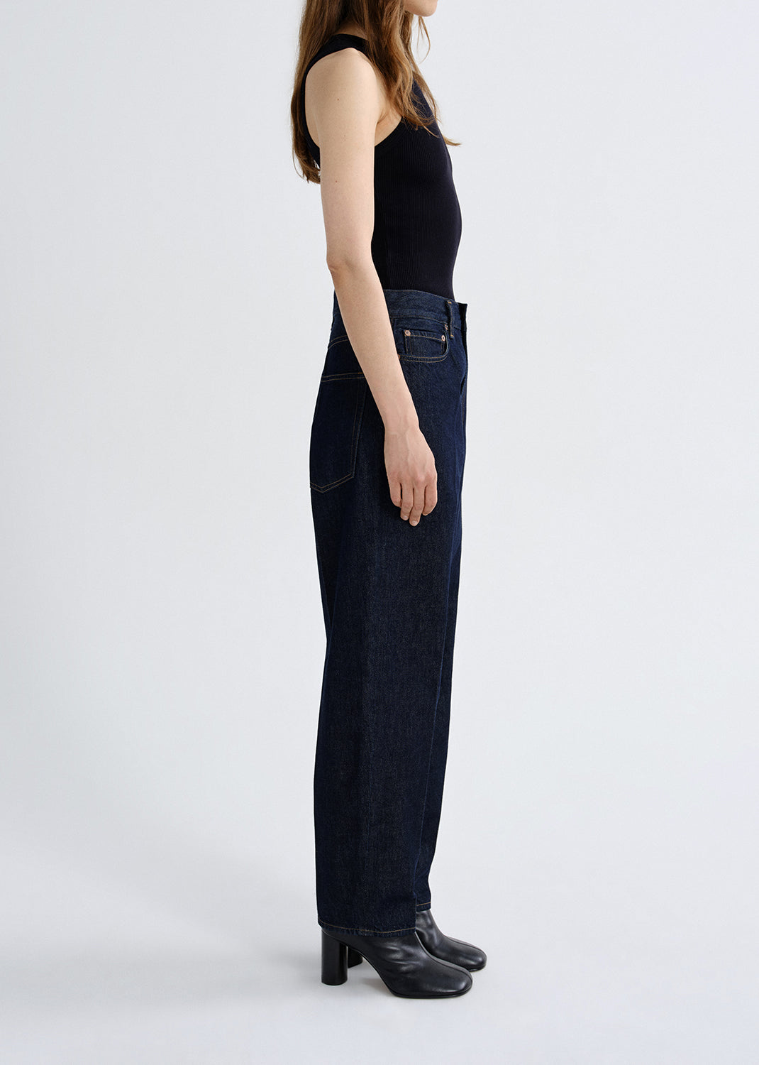 Person wearing dark blue jeans and black shoes on a grey background