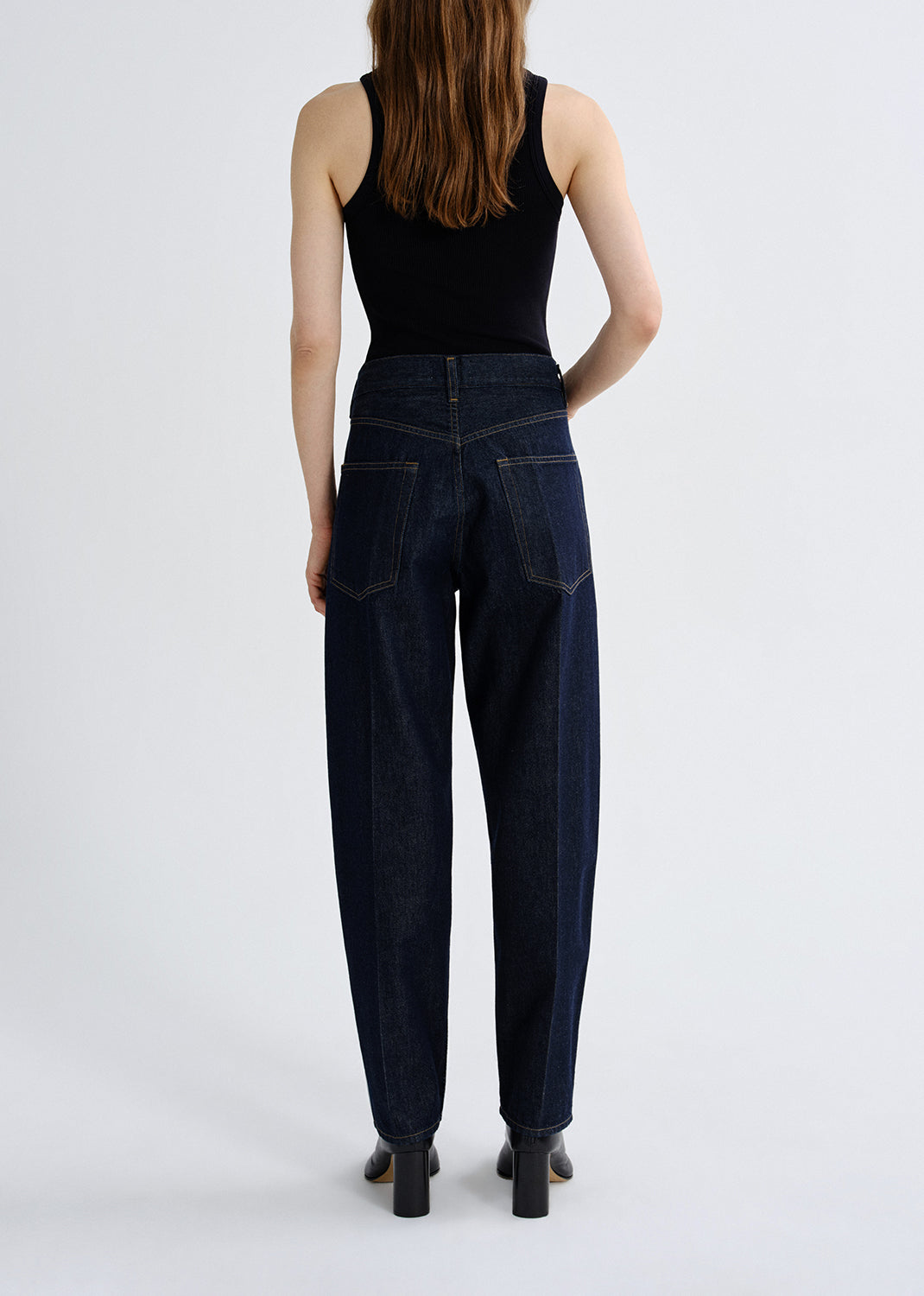Person wearing dark blue jeans and a black top on a grey background