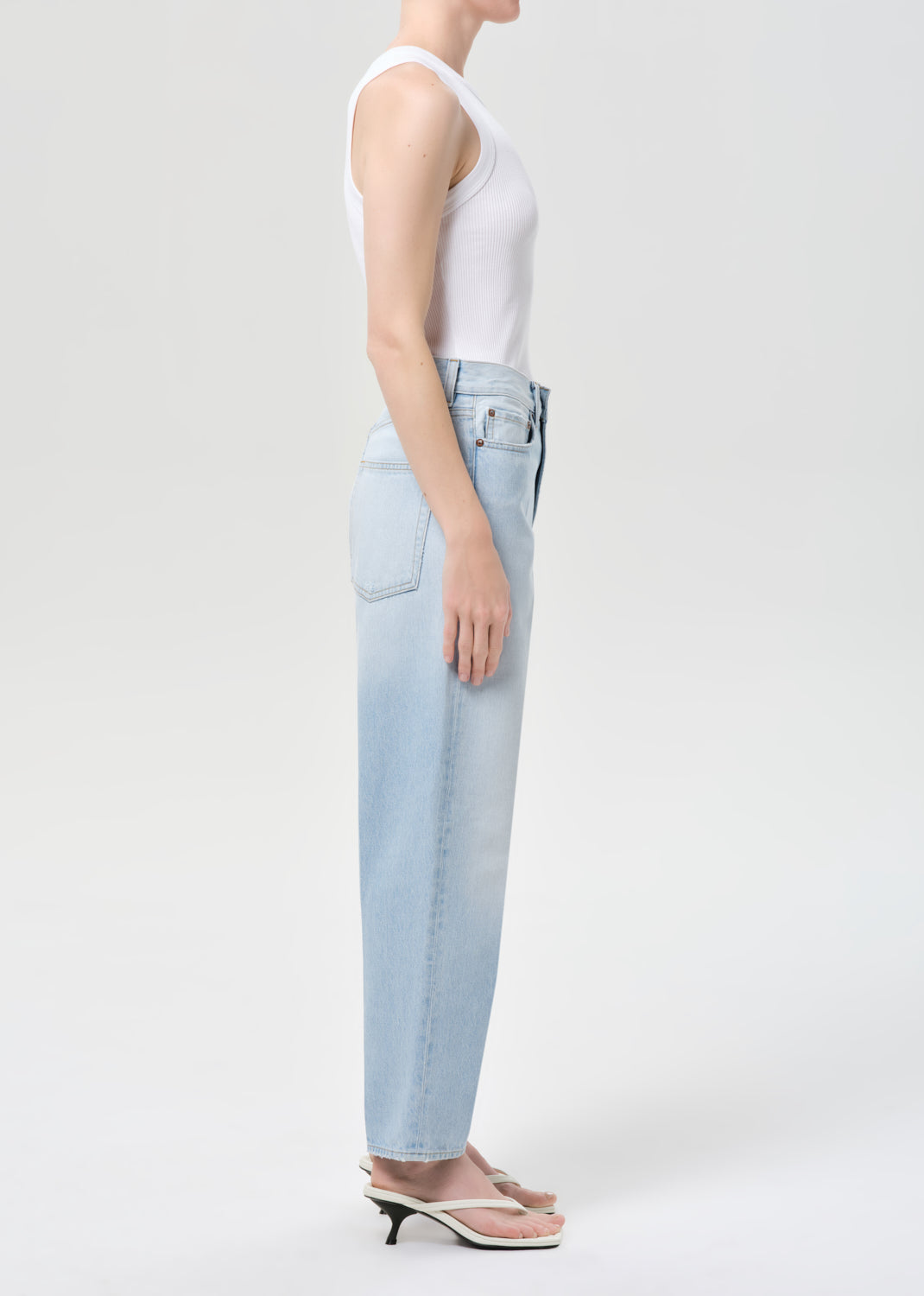 Person wearing light blue jeans and a white tank top on a plain background