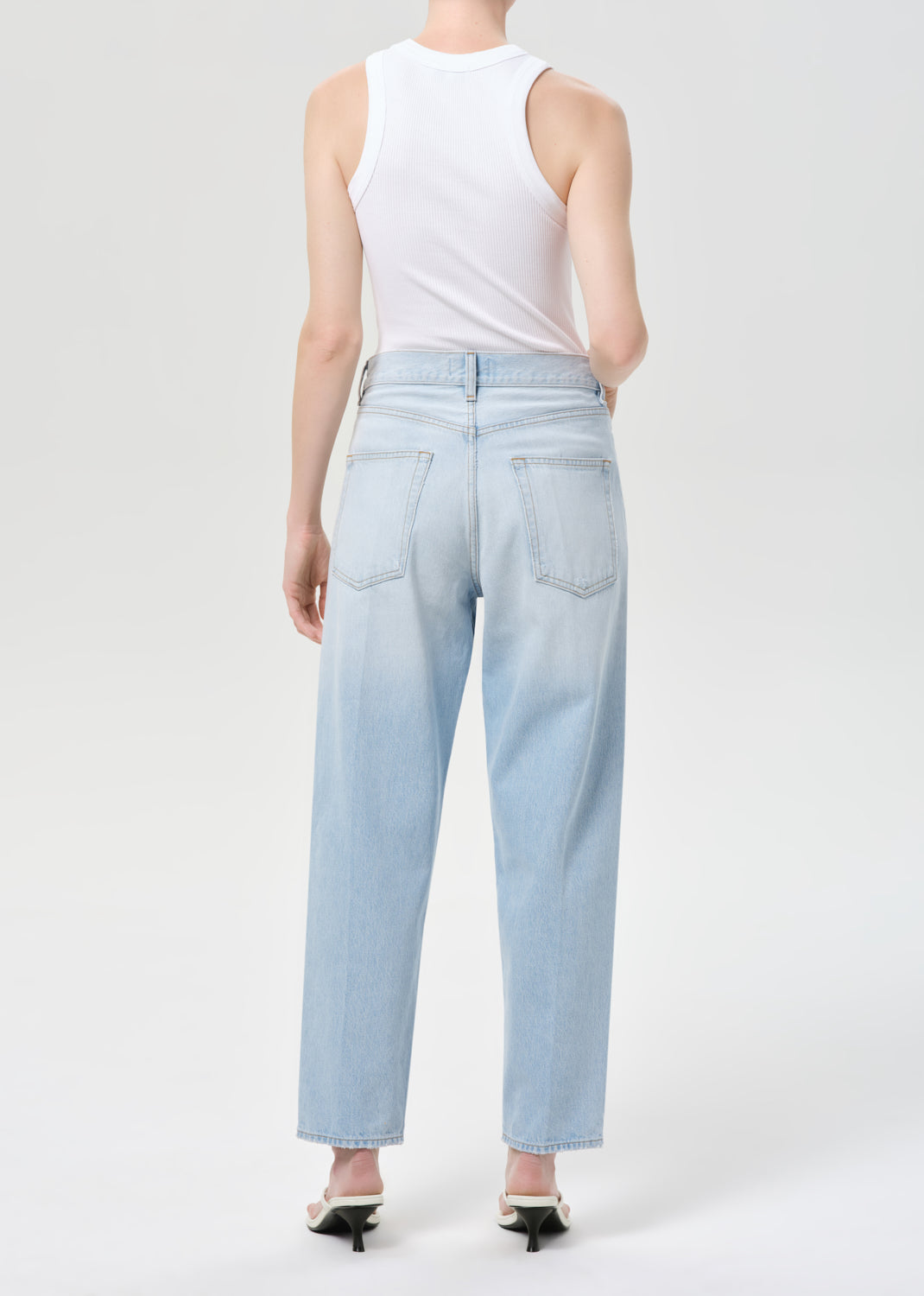 Person wearing light blue jeans and a white sleeveless top on a white background