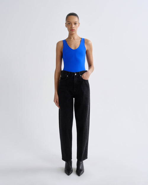 Person wearing a blue tank top and black pants on a white background