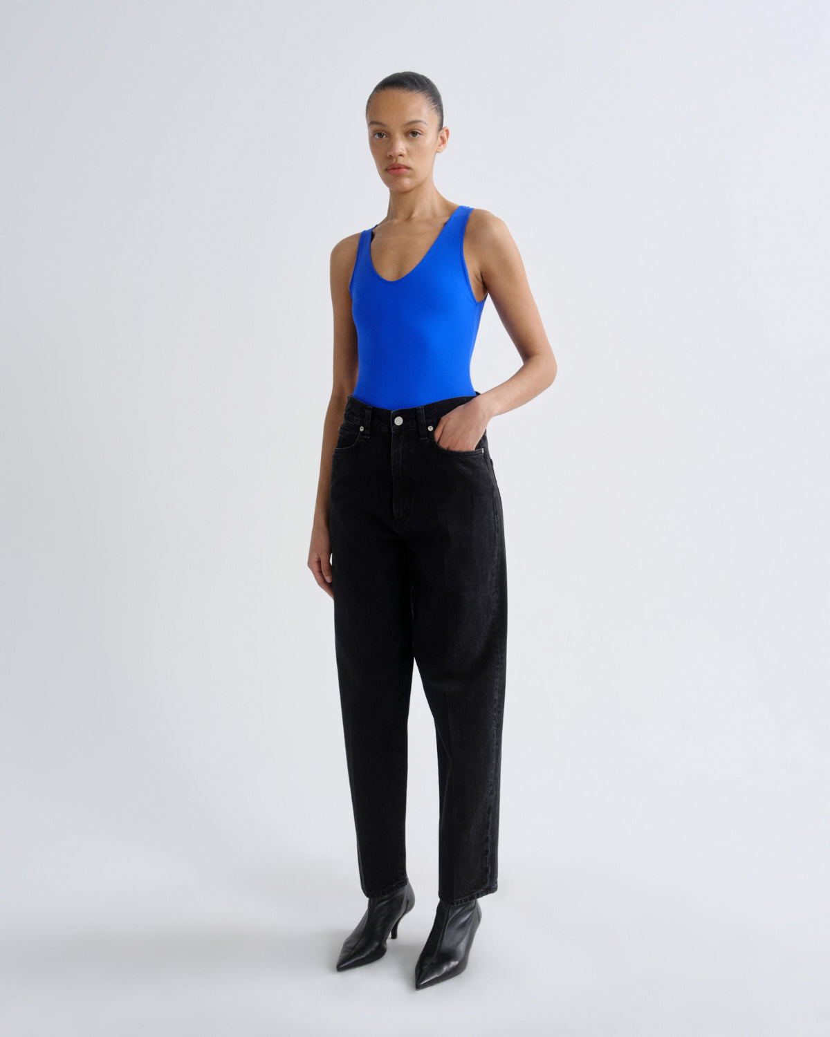 Person wearing a blue tank top and black pants on a white background
