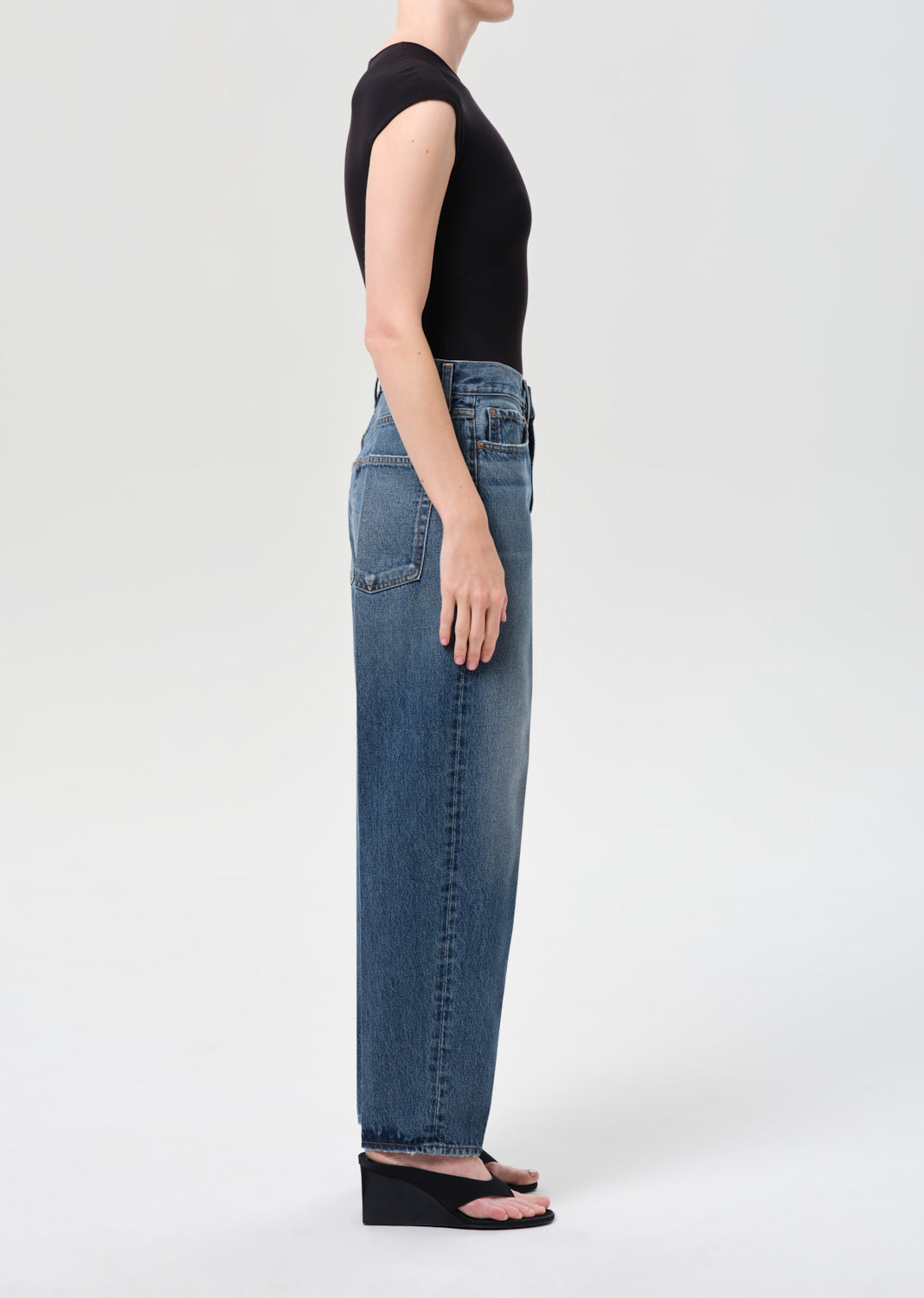 Person wearing blue jeans and a black top on a white background