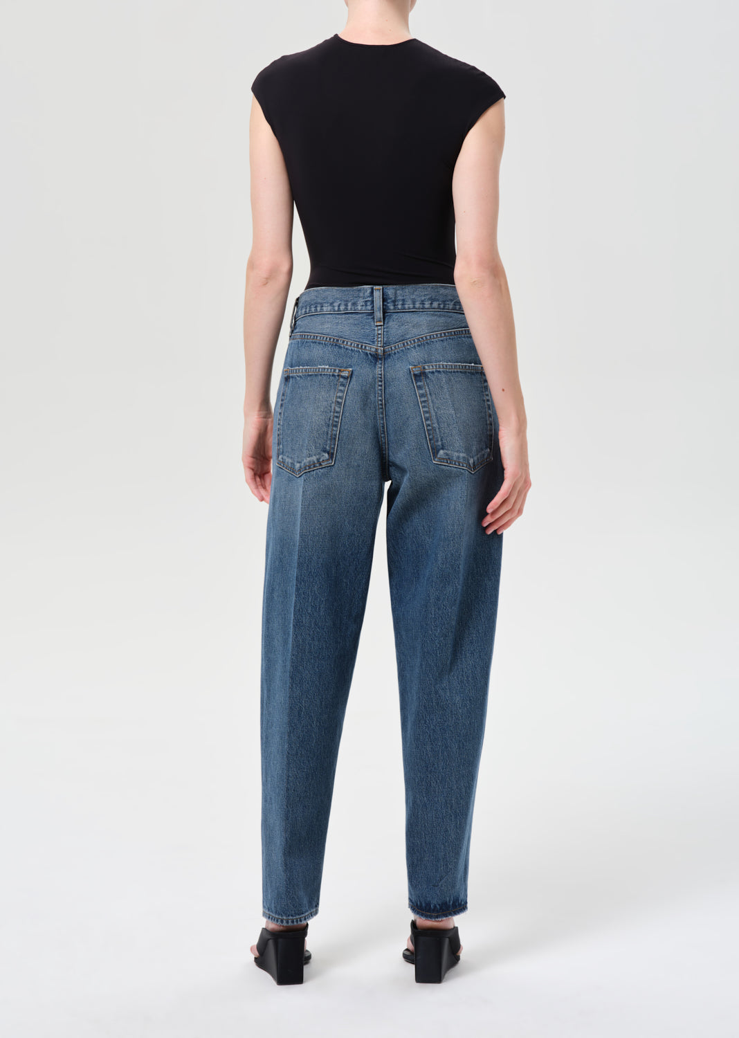 Person wearing blue jeans and a black top on a white background