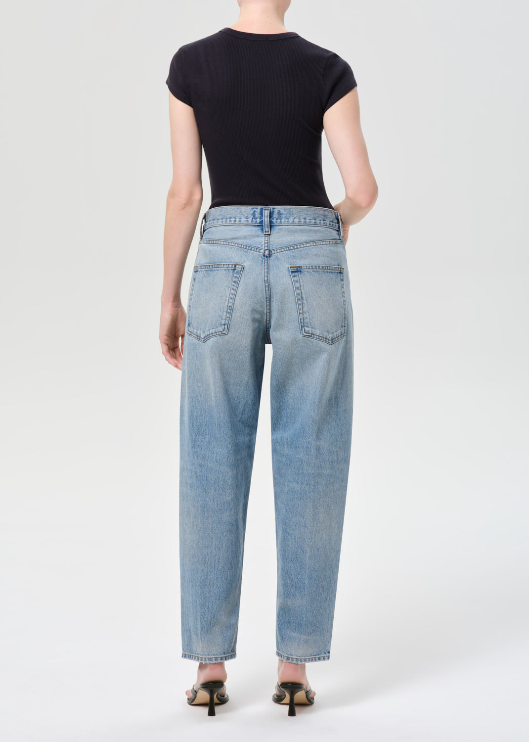 Person wearing light blue jeans and a black top on a white background