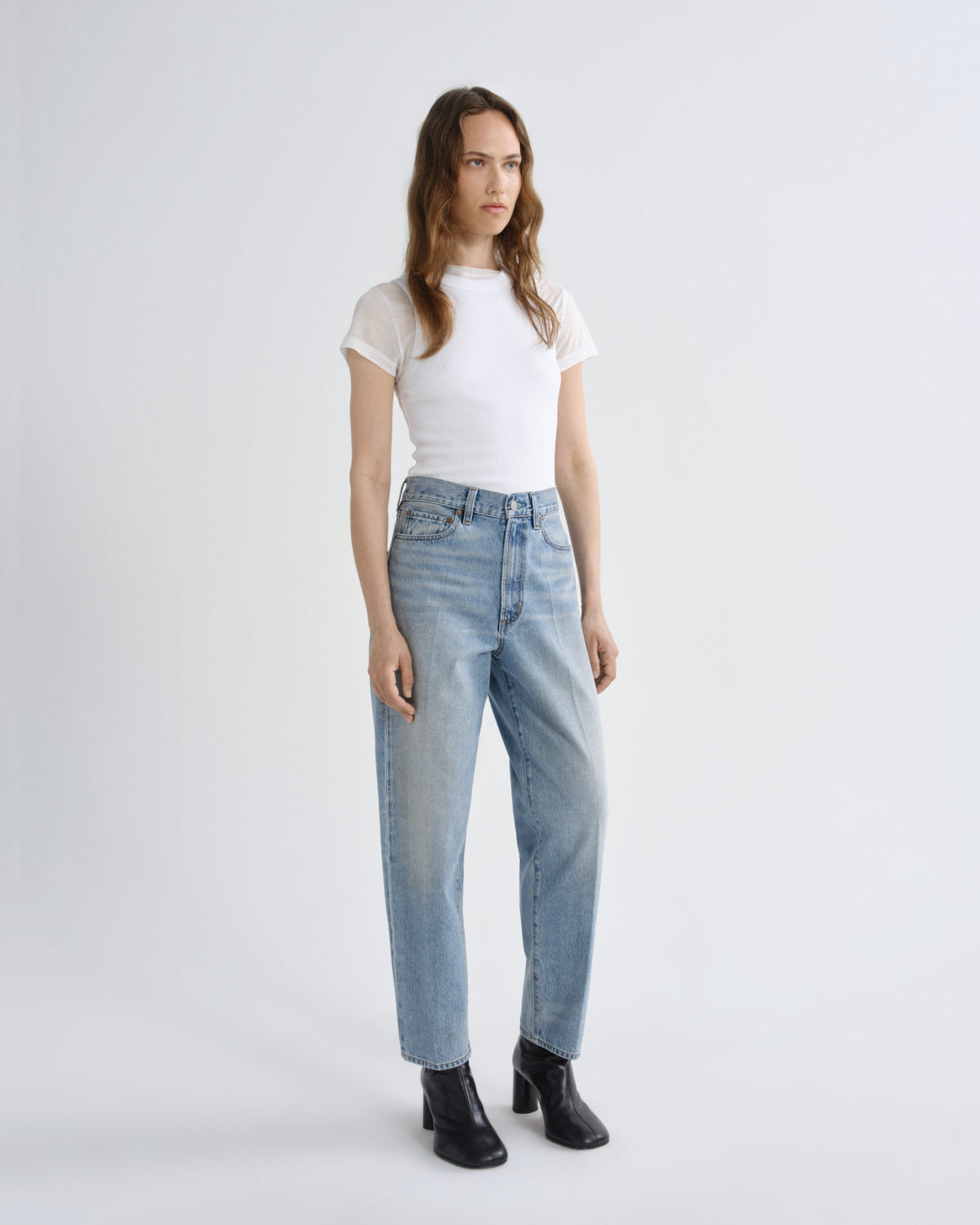 Woman wearing a white t-shirt and light blue jeans on a plain background
