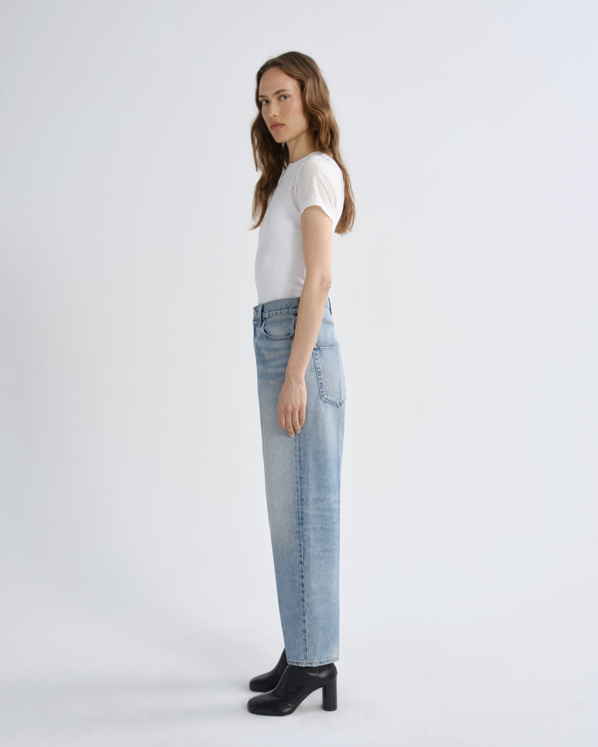 Woman wearing light blue jeans and a white shirt on a white background