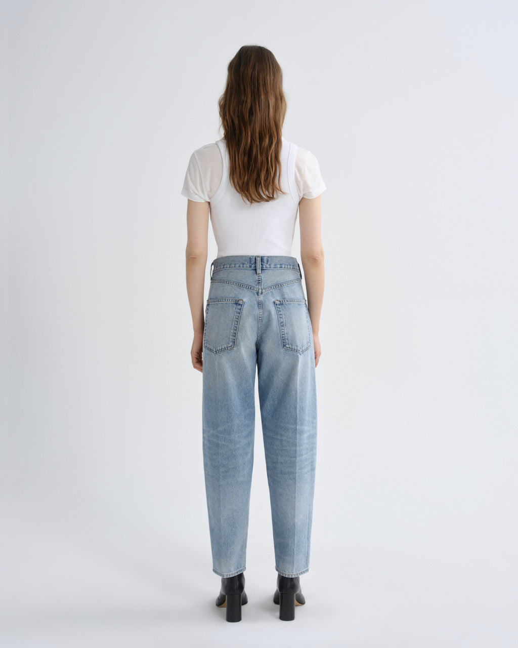 Person wearing light blue jeans and a white shirt on a plain background