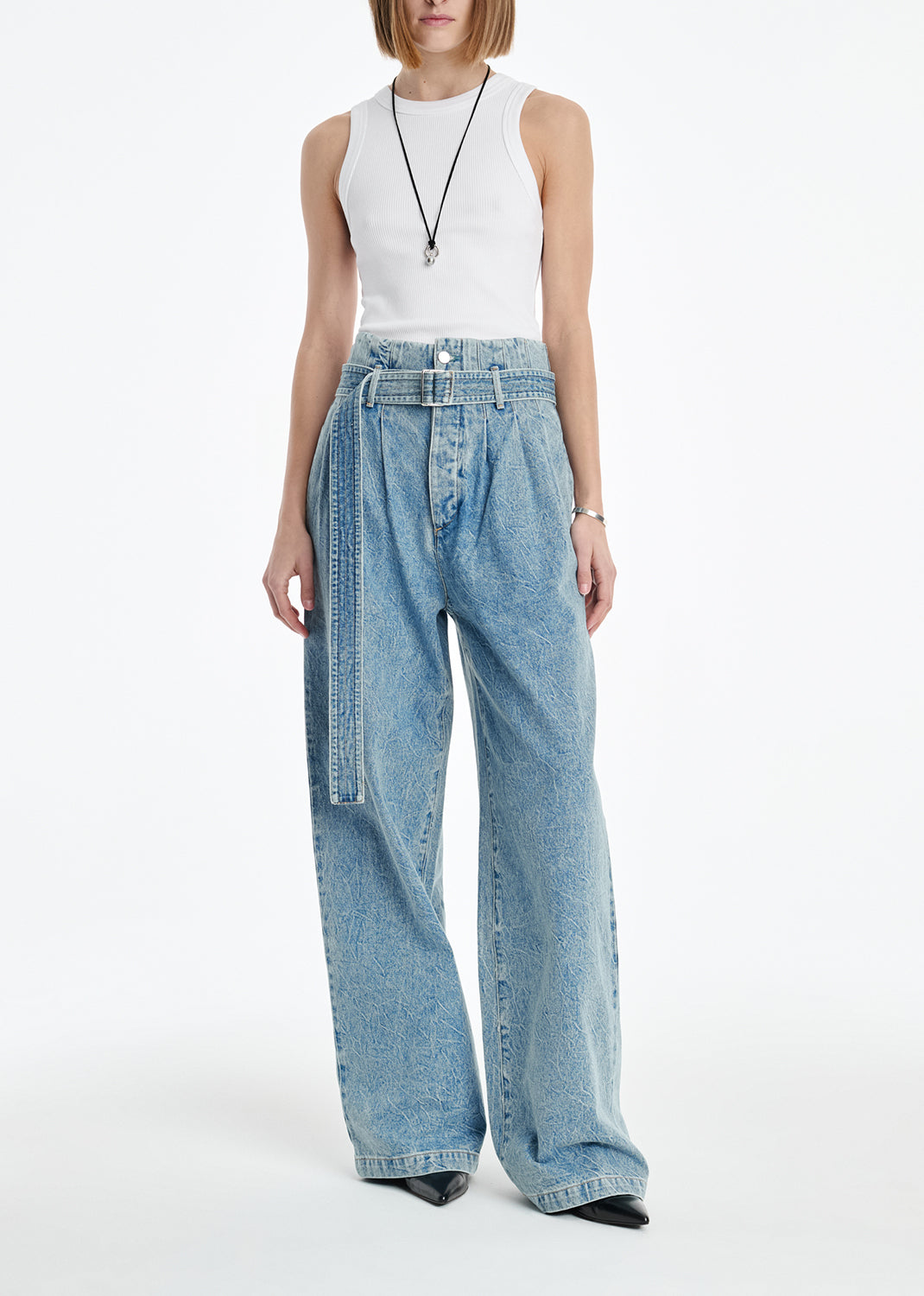 Person wearing a white sleeveless top and light blue jeans on a white background