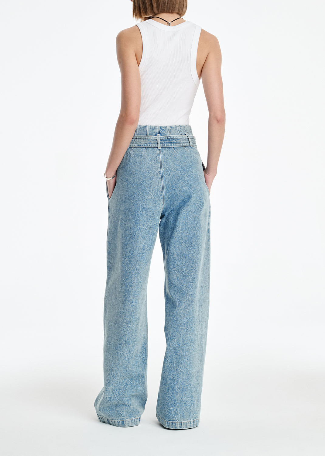 Person wearing light blue jeans and a white sleeveless top on a white background