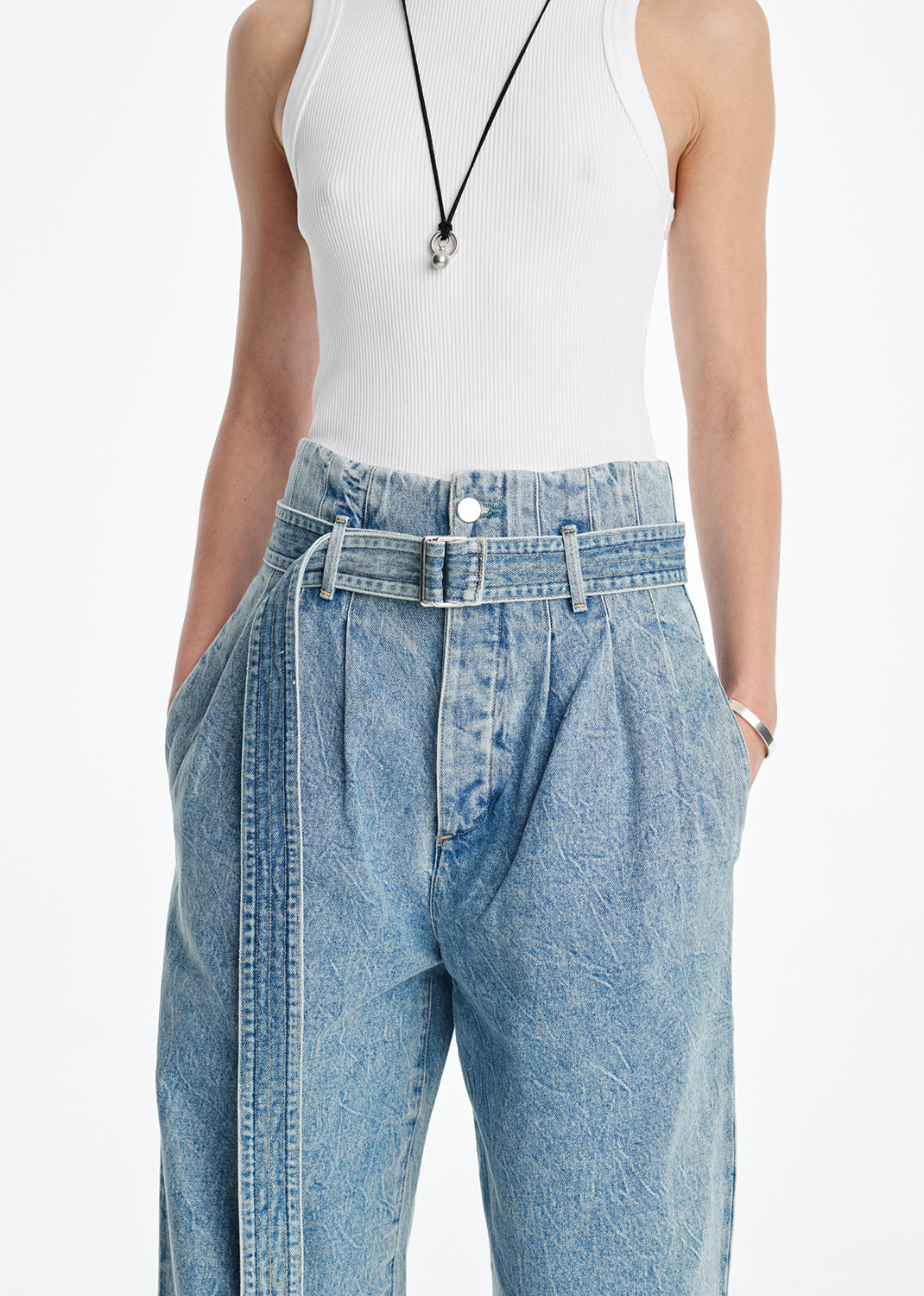 Person wearing a white tank top and light blue denim pants on a white background