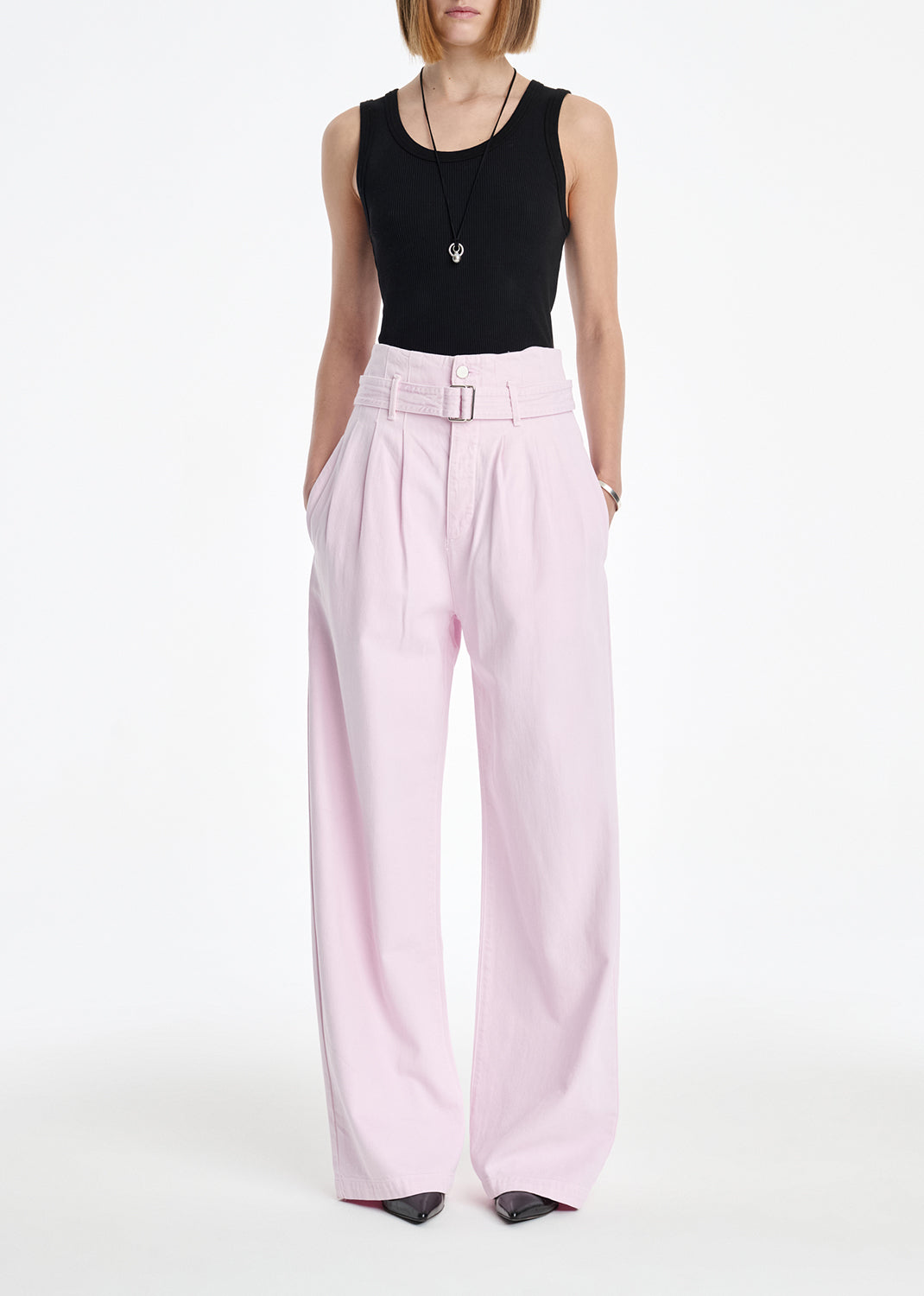 Person wearing a black sleeveless top and light pink pants on a white background