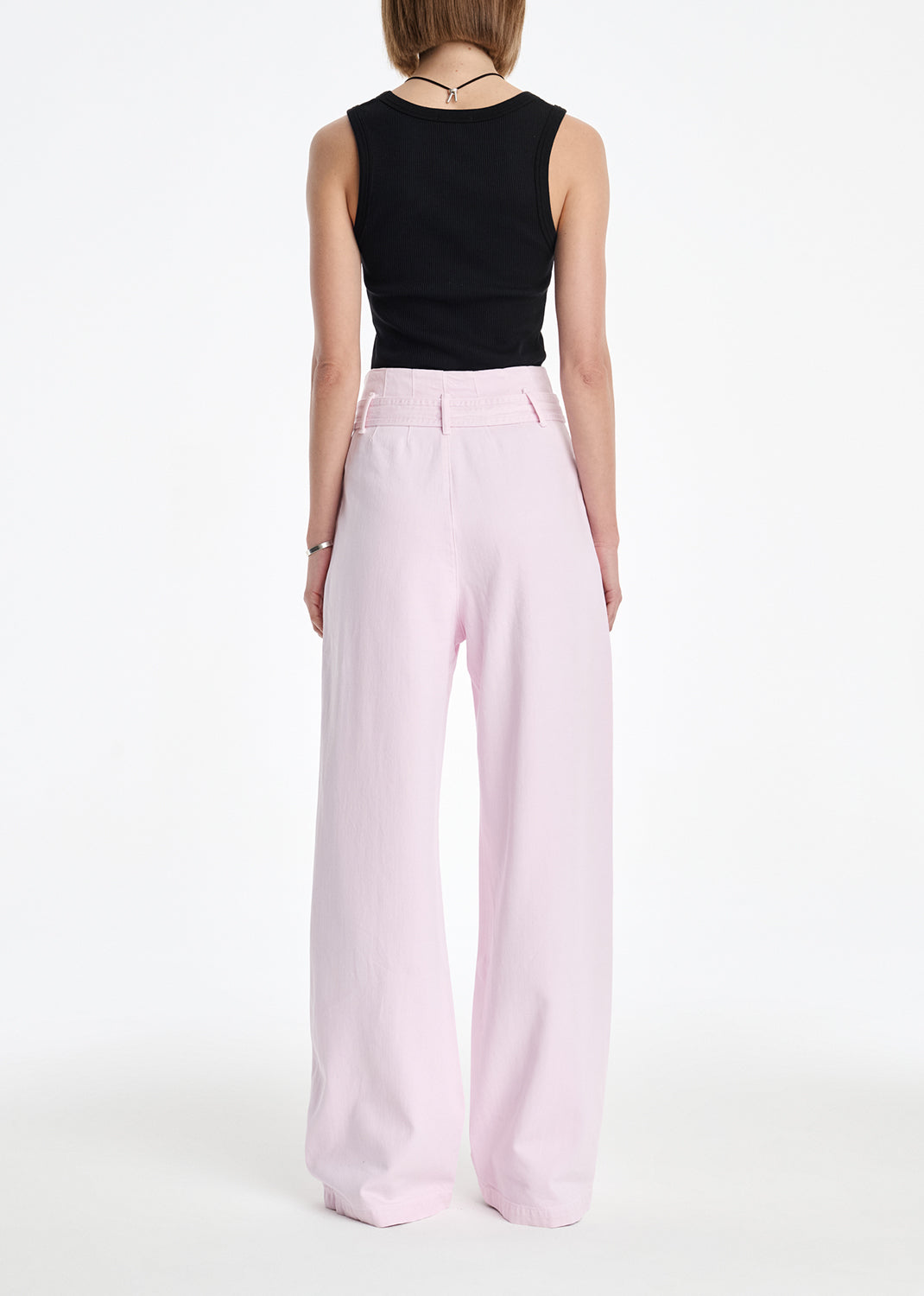 Person wearing a black sleeveless top and light pink wide-leg pants on a white background