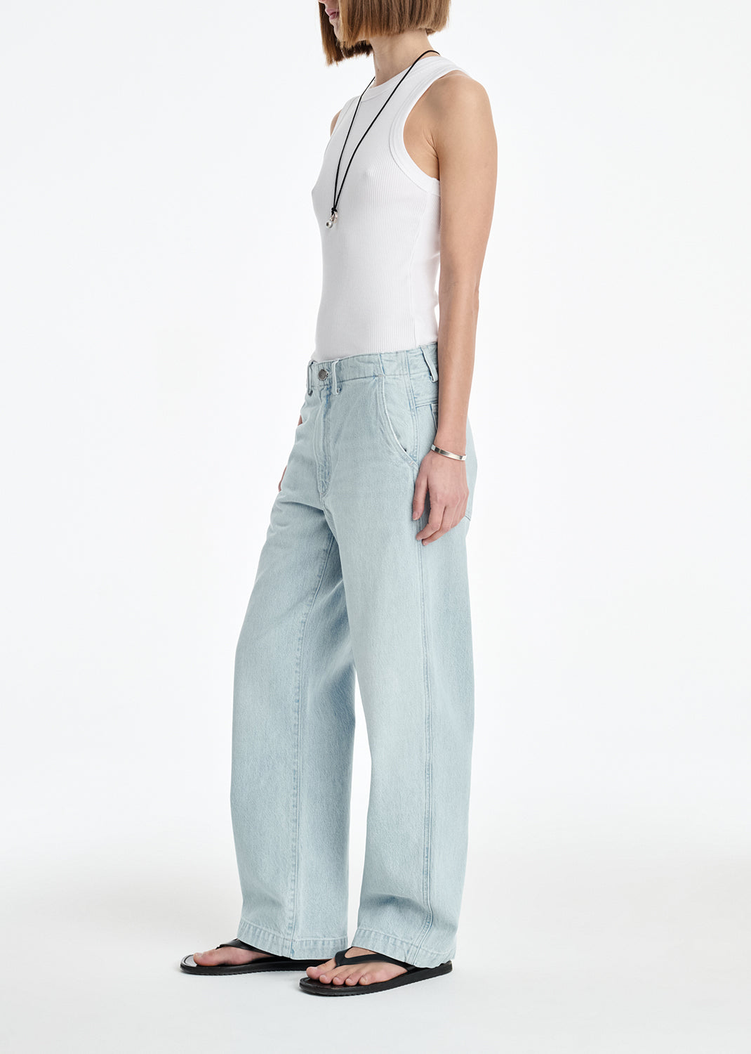 Person wearing a white sleeveless top and light blue jeans on a white background