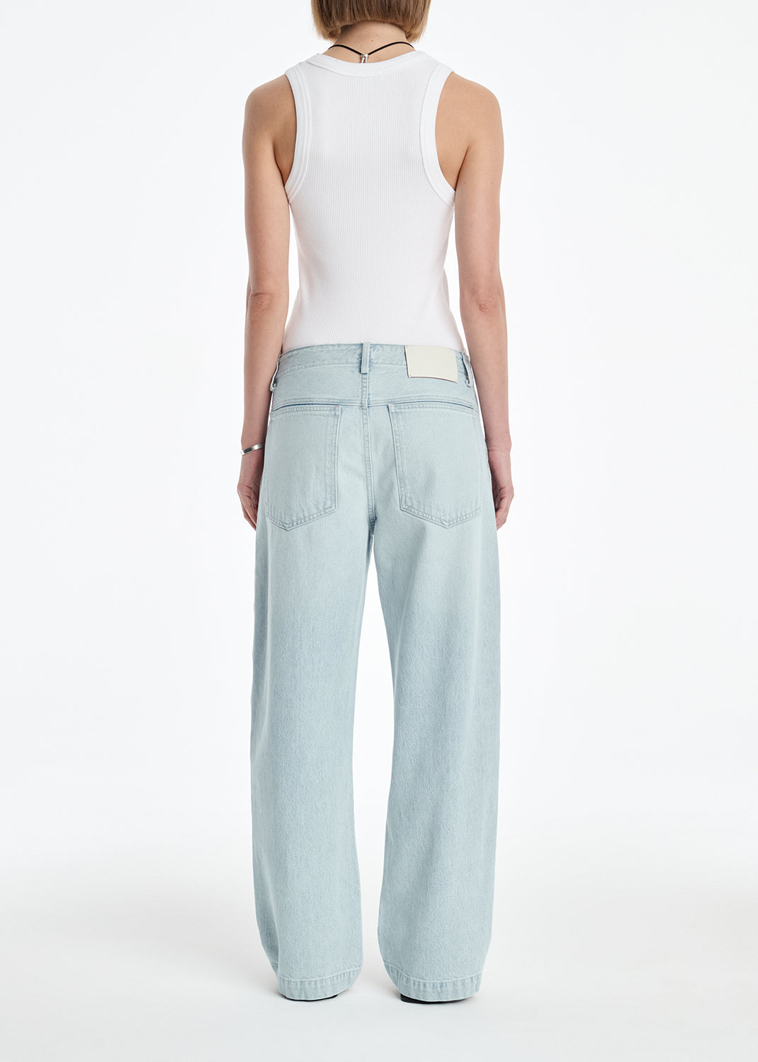 Person wearing light blue jeans and a white sleeveless top on a white background