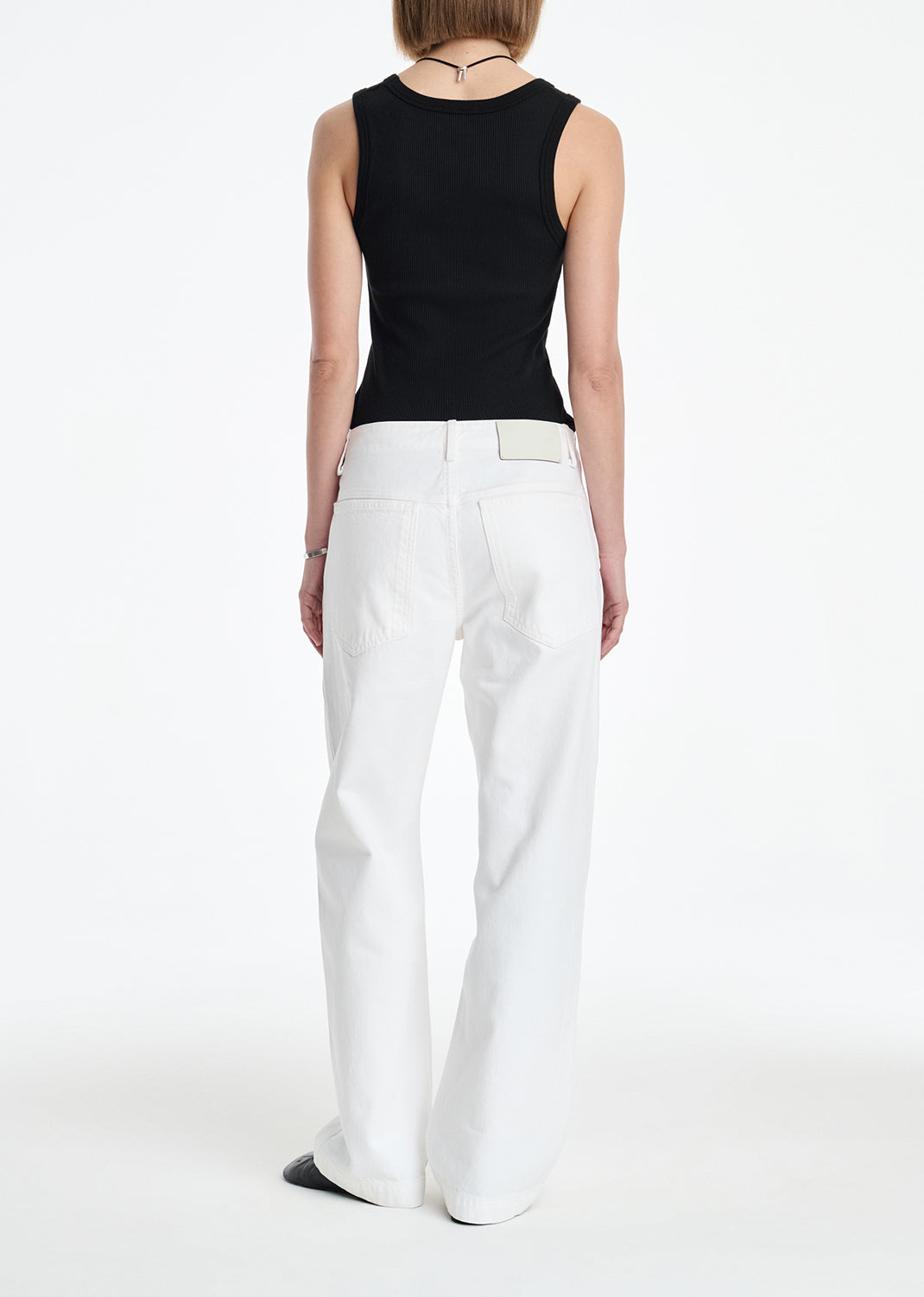 Person wearing a black sleeveless top and white pants on a white background