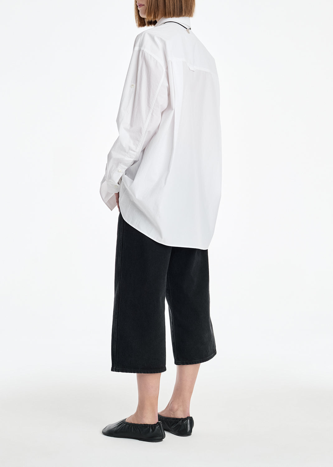 Person wearing a white oversized shirt and black pants on a white background