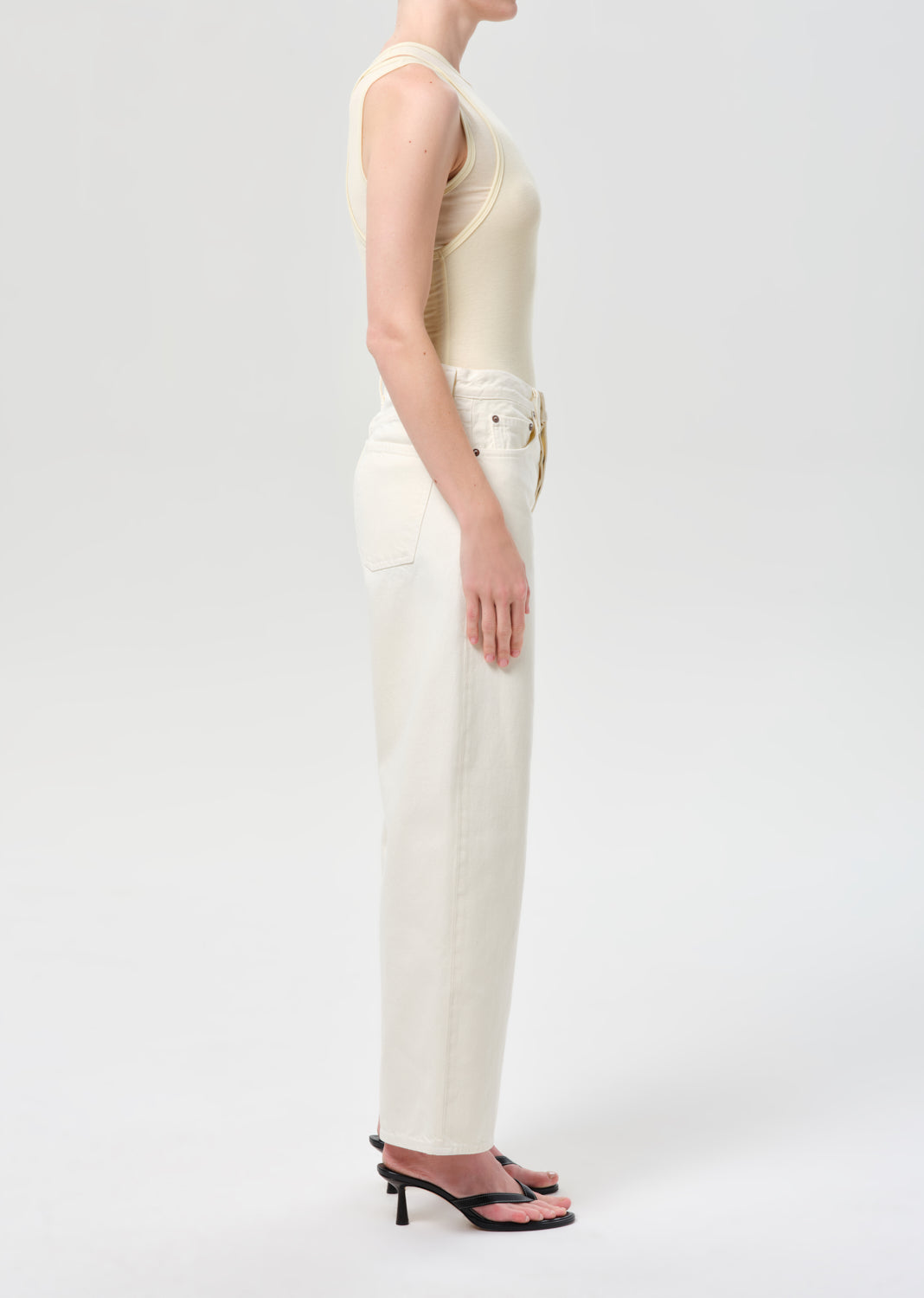 Person wearing a cream sleeveless top and white pants on a light gray background