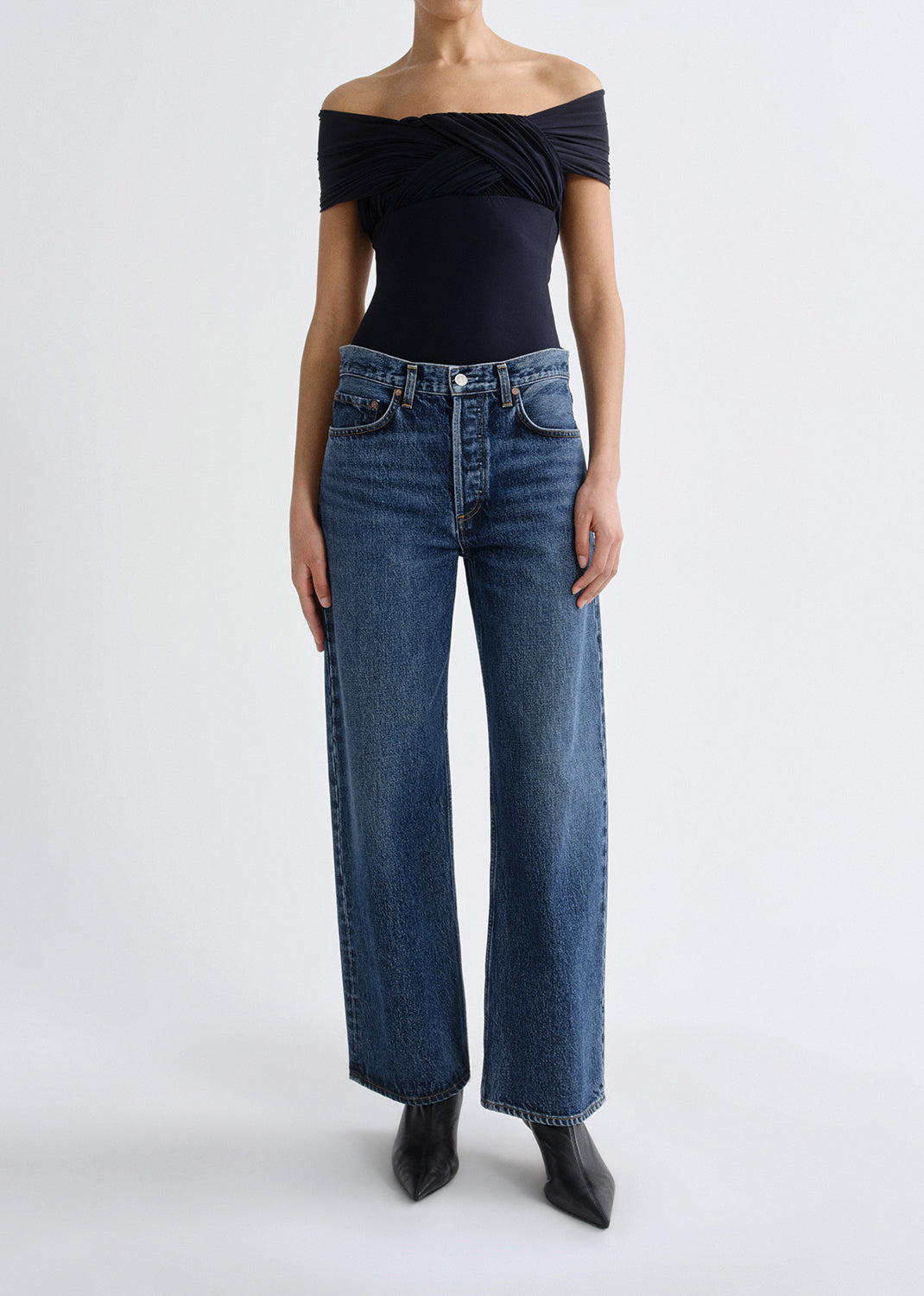 Person wearing a black off-shoulder top and blue jeans on a grey background