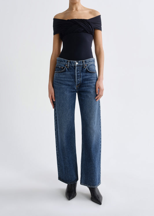 Person wearing a black off-shoulder top and blue jeans on a grey background