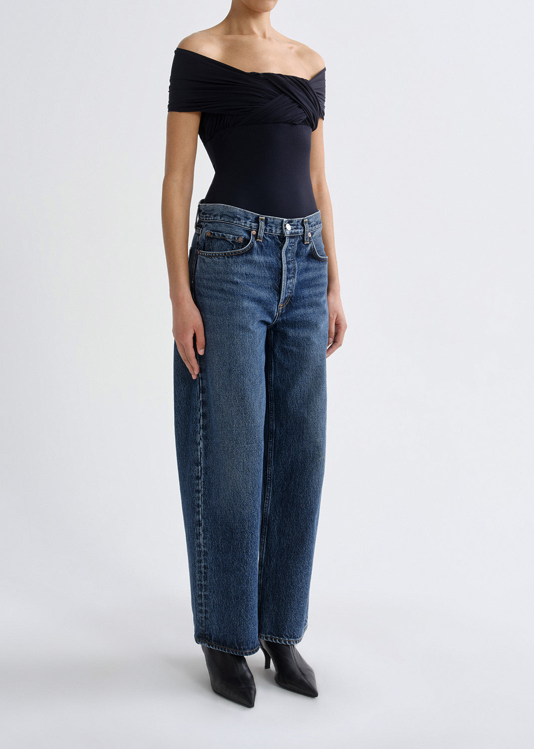 Person wearing a black off-shoulder top and blue jeans on a grey background