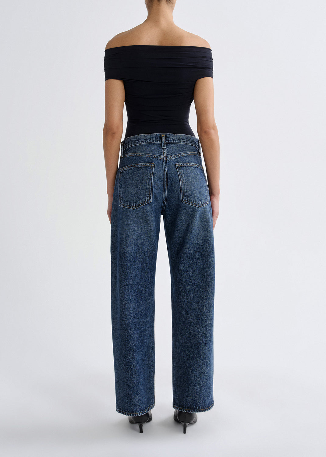 Person wearing blue jeans and a black off-shoulder top on a grey background