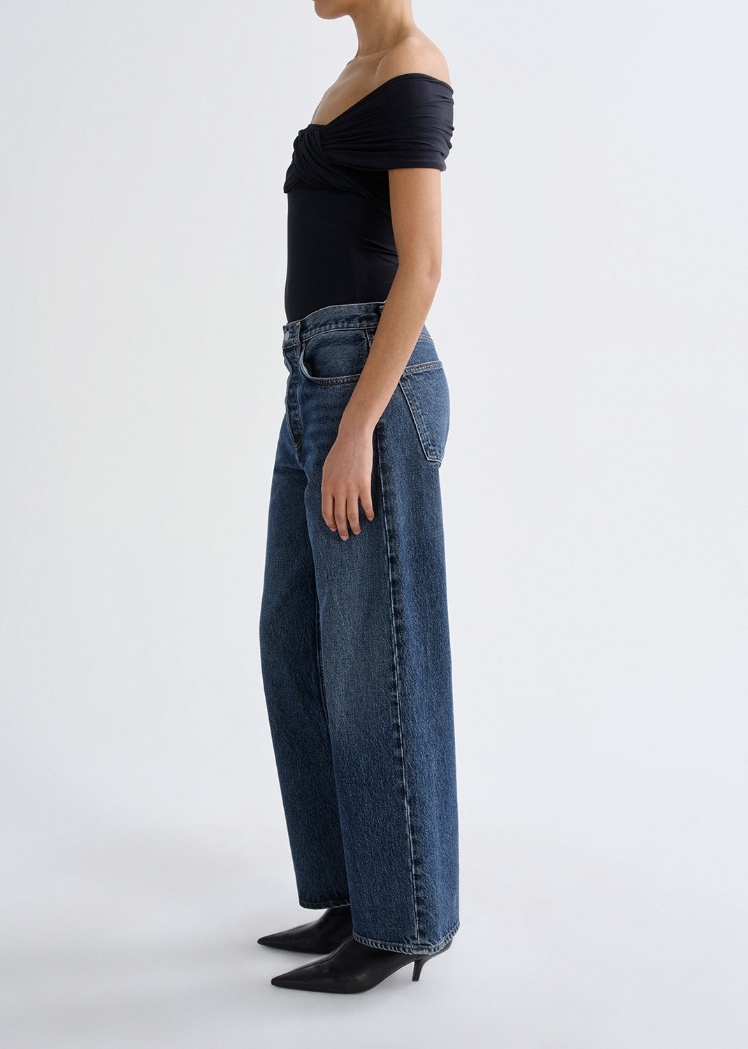 Person wearing a black top and blue jeans on a grey background