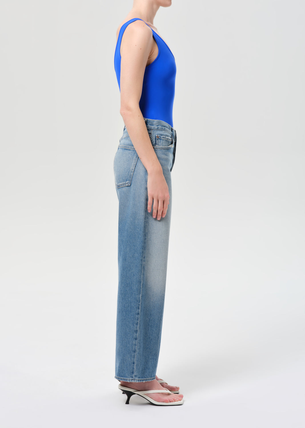 Person wearing blue tank top and light blue jeans on a white background