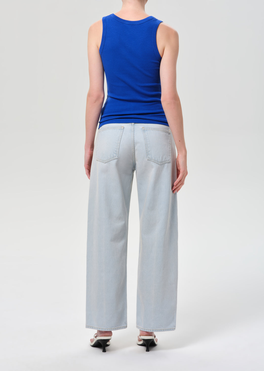 Person wearing a blue sleeveless top and light gray wide-leg pants on a white background