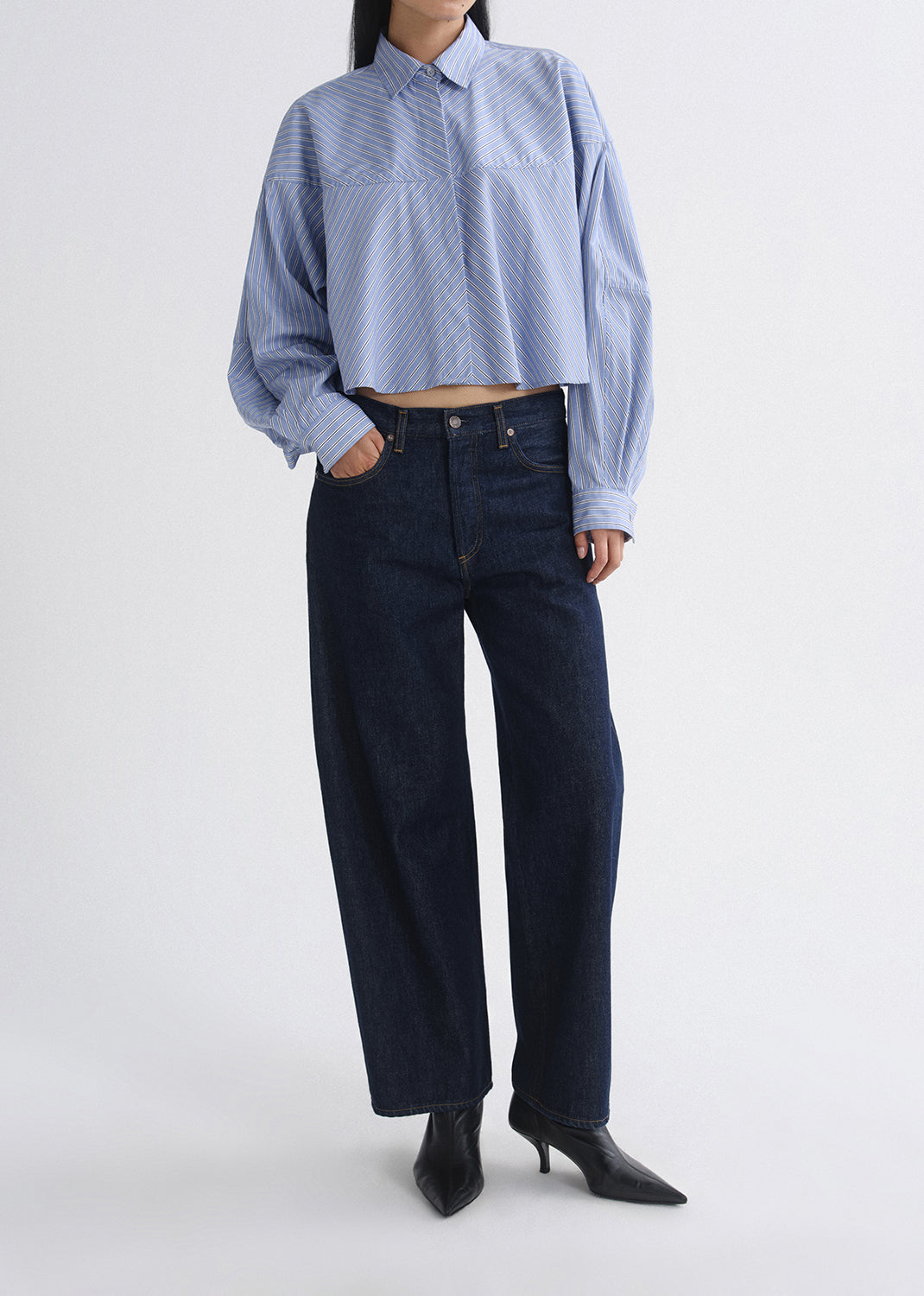 Person wearing a blue striped shirt and dark jeans on a grey background