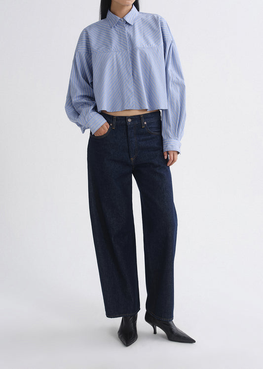 Person wearing a blue striped shirt and dark jeans on a grey background
