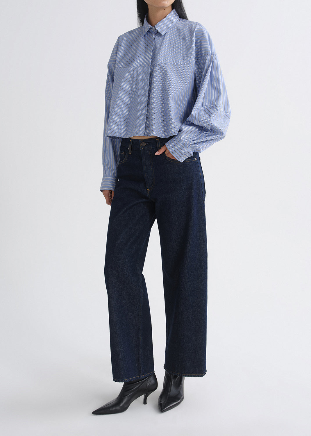 Person wearing a blue checkered shirt and dark jeans on a grey background