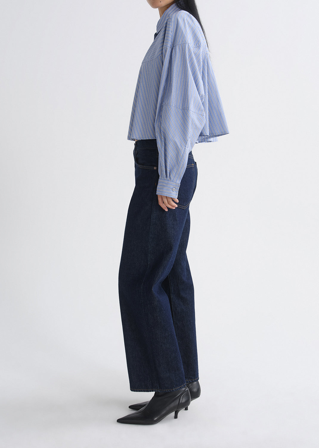 Person wearing a light blue striped shirt and dark blue jeans on a grey background