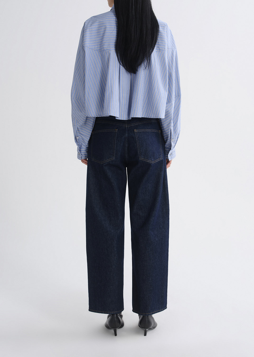 Person wearing a light blue striped shirt and dark blue jeans on a grey background