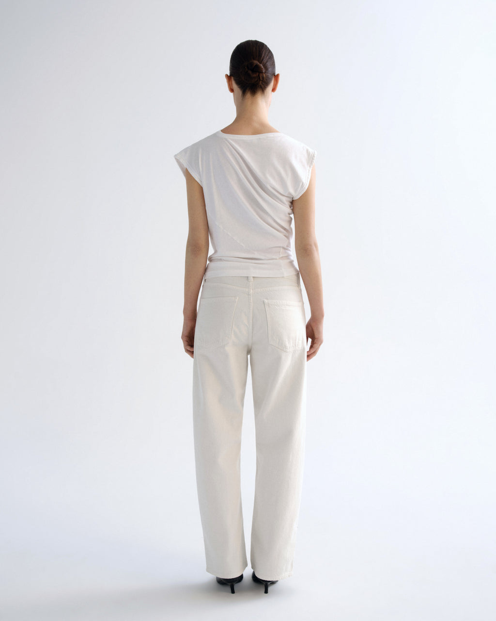 A model viewed from the back wearing a white draped, cap-sleeve top and matching white wide-leg trousers against a clean white studio background.