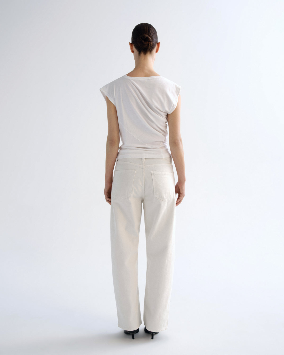 A model viewed from the back wearing a white draped, cap-sleeve top and matching white wide-leg trousers against a clean white studio background.