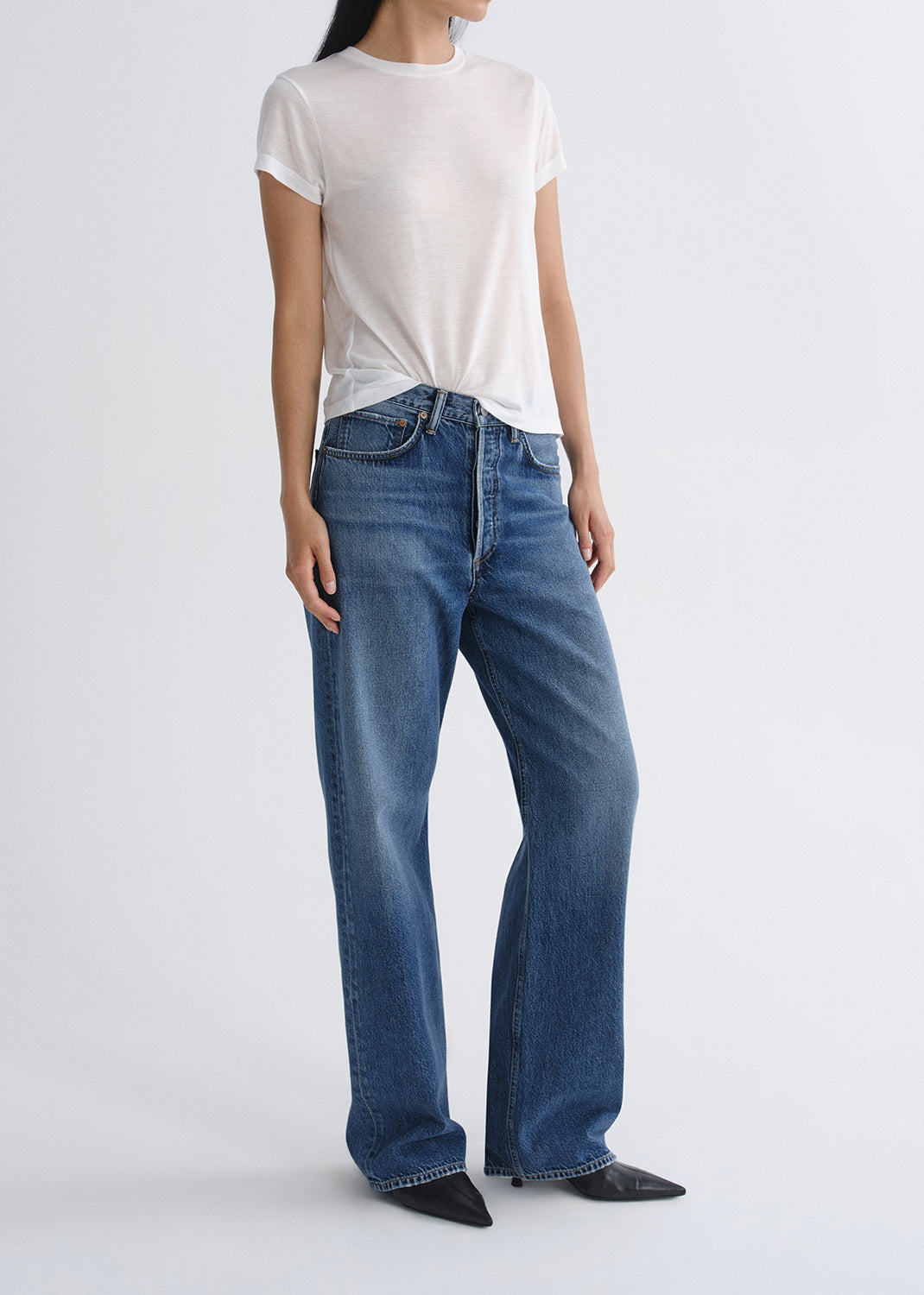 Person wearing a white short sleeve crewneck tee with medium wash wide leg jeans on a grey background.
